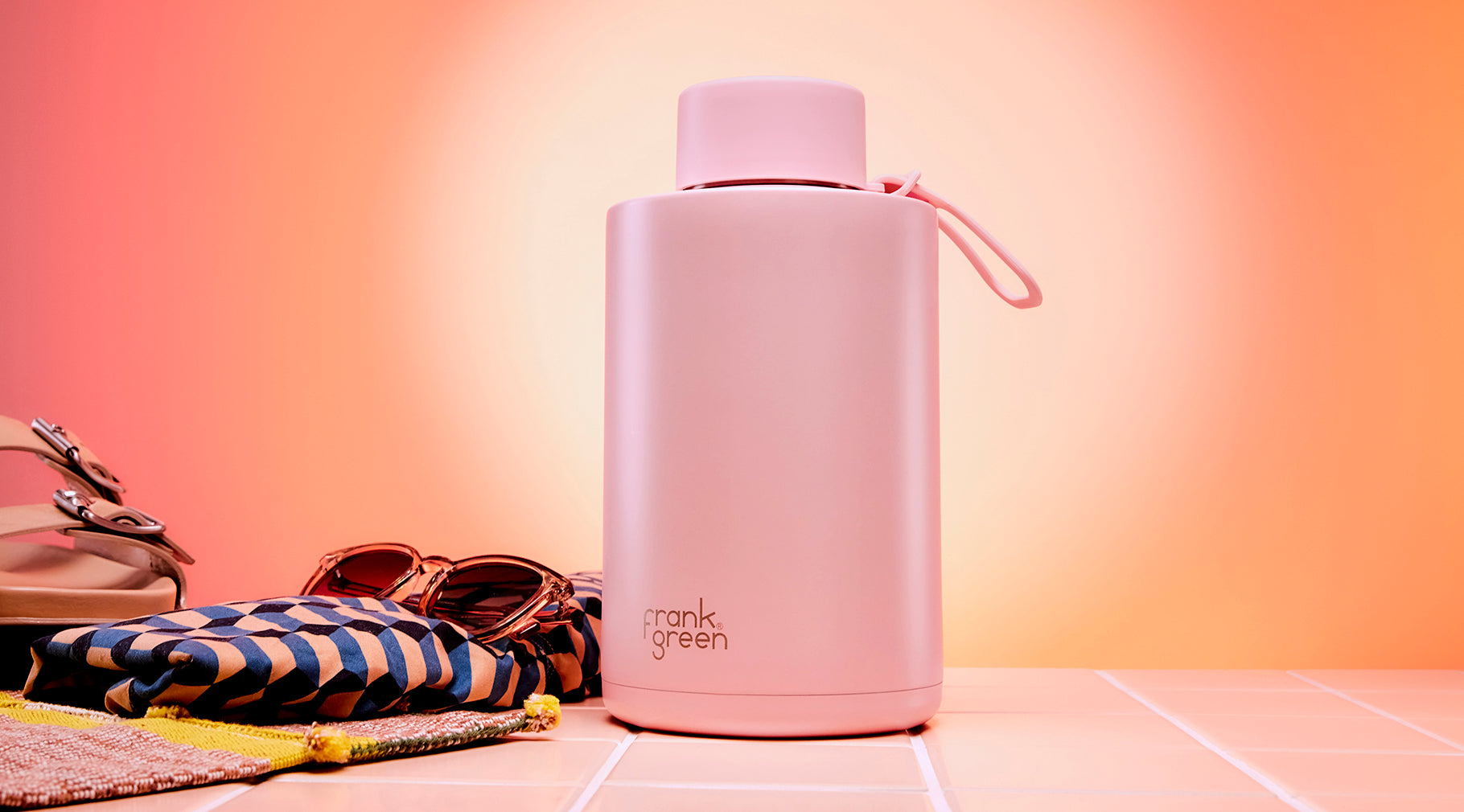 A matte pink insulated water bottle with a matching pink lid and carry loop, standing on a tiled surface. The bottle has the 'frank green' logo printed near the bottom.